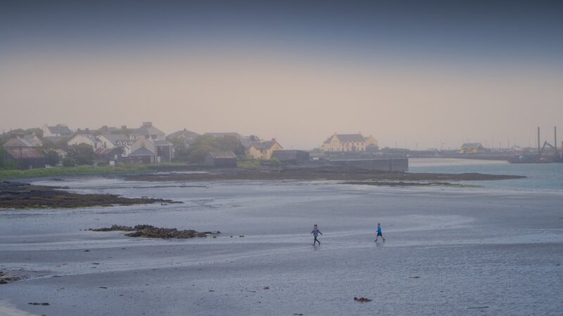 Two people walking along a misty beach by the sea