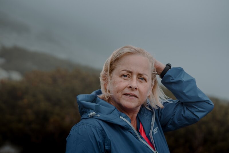 A woman in her fifties standing outdoors in a blue jacket, looking thoughtful