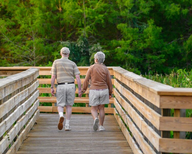 An older couple holding hands as they walk together across a wooden boardwalk