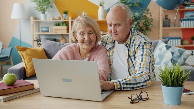 An older couple smiling while looking at a laptop together at home