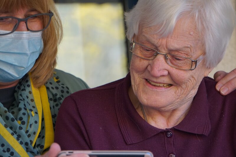 A community nurse sitting with an older woman at home, looking at a tablet together