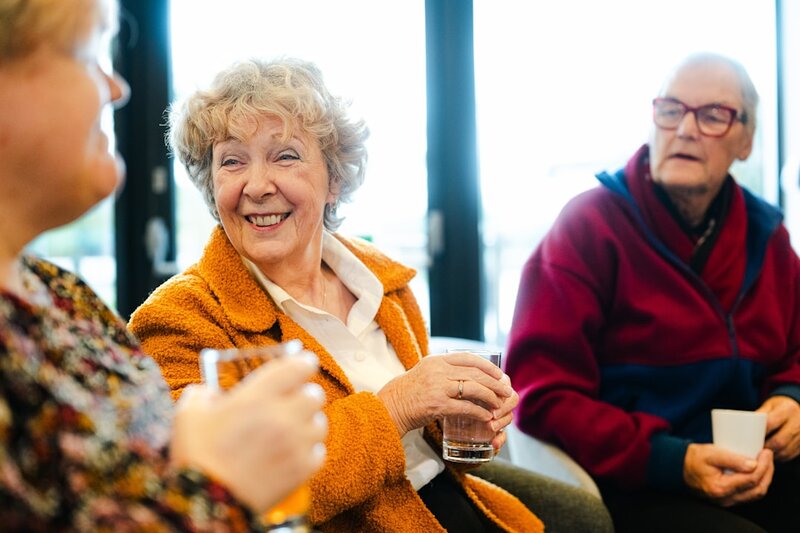 Older adults chatting and smiling together, one wearing glasses