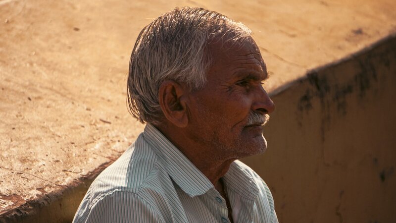 Older man in profile, ear visible, sitting outdoors in warm sunlight