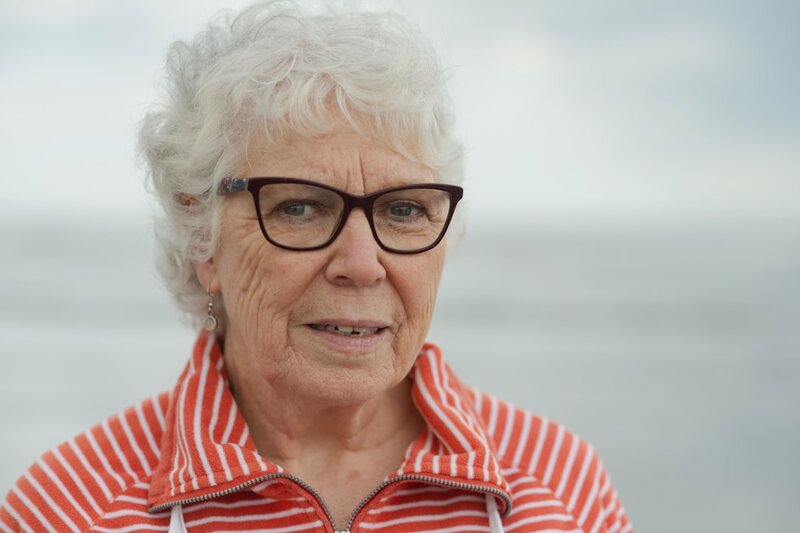Older woman wearing glasses smiling by the coast