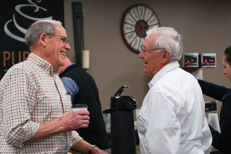 Two older men chatting warmly over coffee at a community gathering