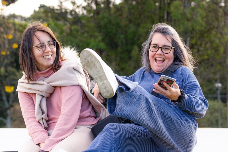 Two women laughing together outdoors on a bright day