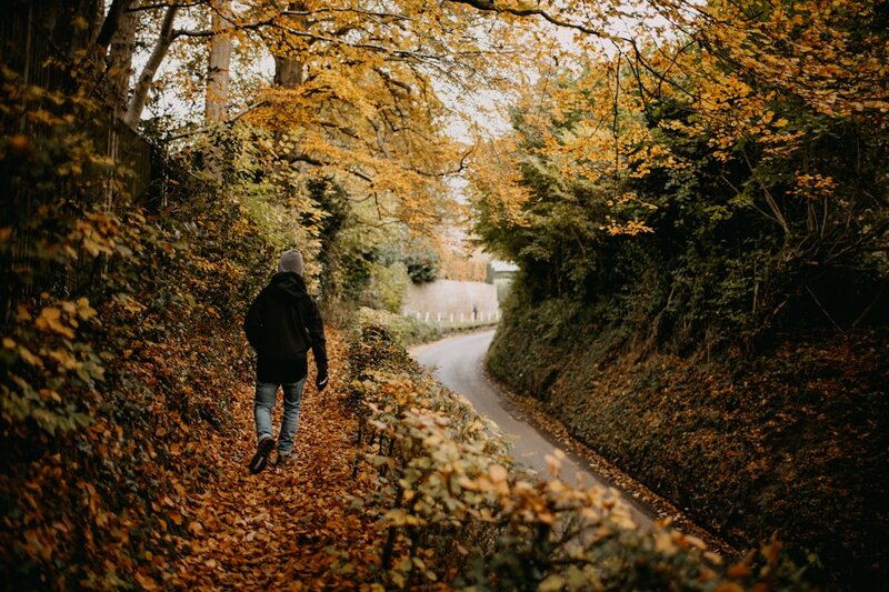 A person walking alone along a quiet leaf-covered country lane in autumn