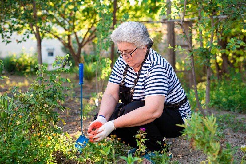 An older woman kneeling in a garden, holding an apple
