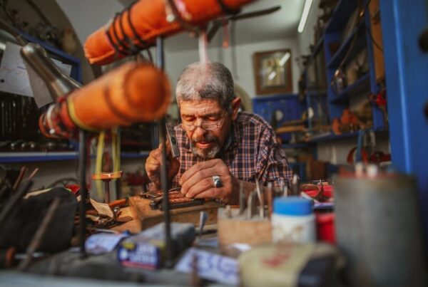 A man in his sixties working on a detailed craft at a workbench in his workshop