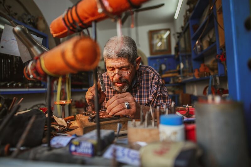 A man in his sixties working on a detailed craft at a workbench in his workshop