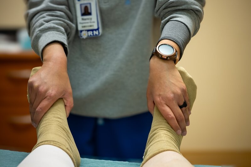 A nurse supporting an older adult's lower legs during a wound care and compression assessment