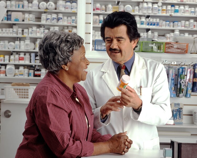 A pharmacist explaining a medicine to an older woman across a pharmacy counter