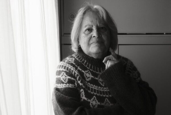 An older woman in a patterned jumper sitting quietly by a window in morning light