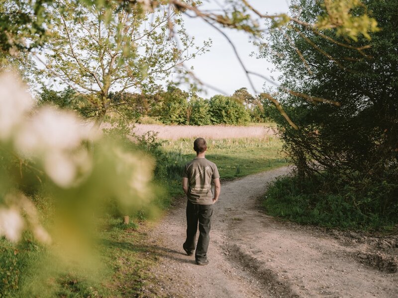 A person walking along a dirt path through a green field in soft evening light