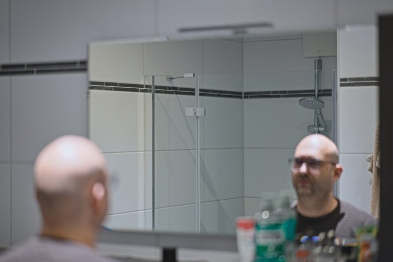 A man looking closely at his own reflection in a bathroom mirror