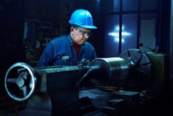 An older man in a hard hat operating a lathe during a night shift
