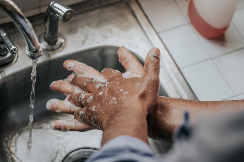 Soapy hands being washed under running water at a kitchen sink