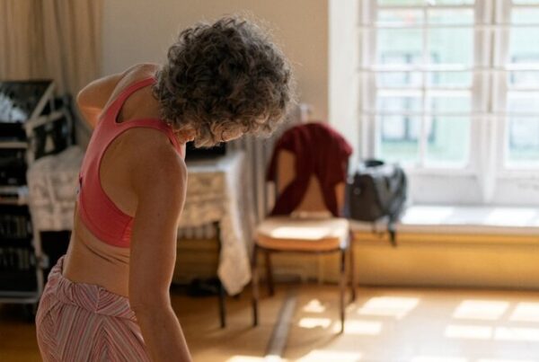Woman with grey hair stretching in a sunlit room