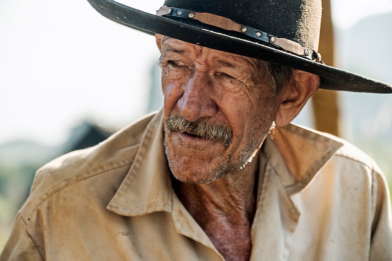 An older man in a wide-brimmed hat outdoors in bright sunshine