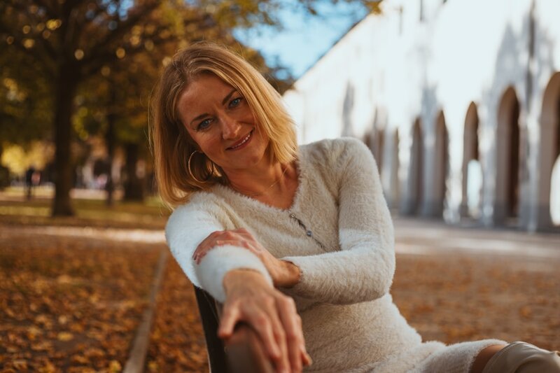 A woman sitting on a park bench among autumn leaves, smiling